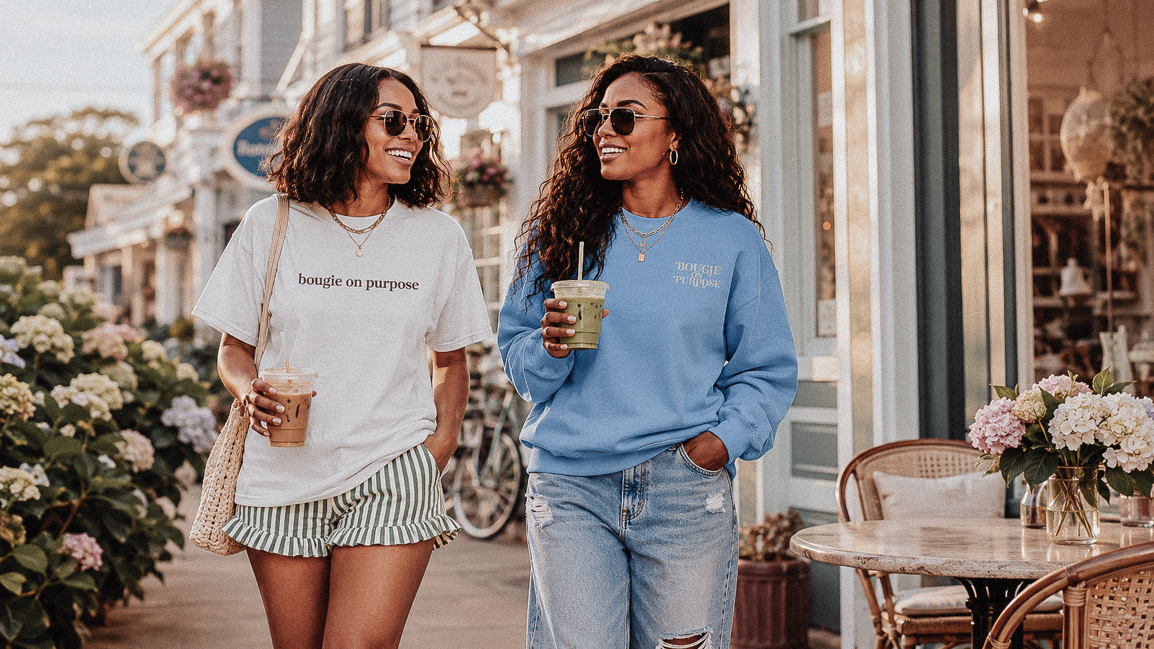 Two women walking outdoors, one holding a drink, with a store and flowers in the background.